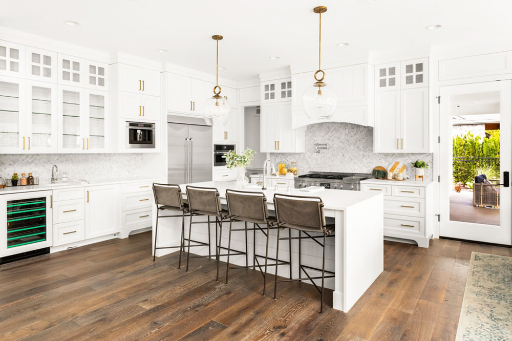 Kitchen Remodeling Beautiful kitchen in new farmhouse style luxury home, with white cabinets, white waterfall island, pendant lights, and hardwood floor. Features wine fridge and stainless steel appliances.